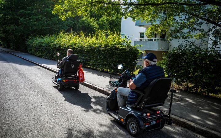 Two Elder Men Moving On an Electric Power Wheelchairs With Lead-aid Battery
